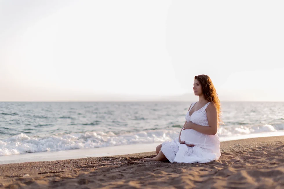 Schwangere Frau in Meditationshaltung am Strand.