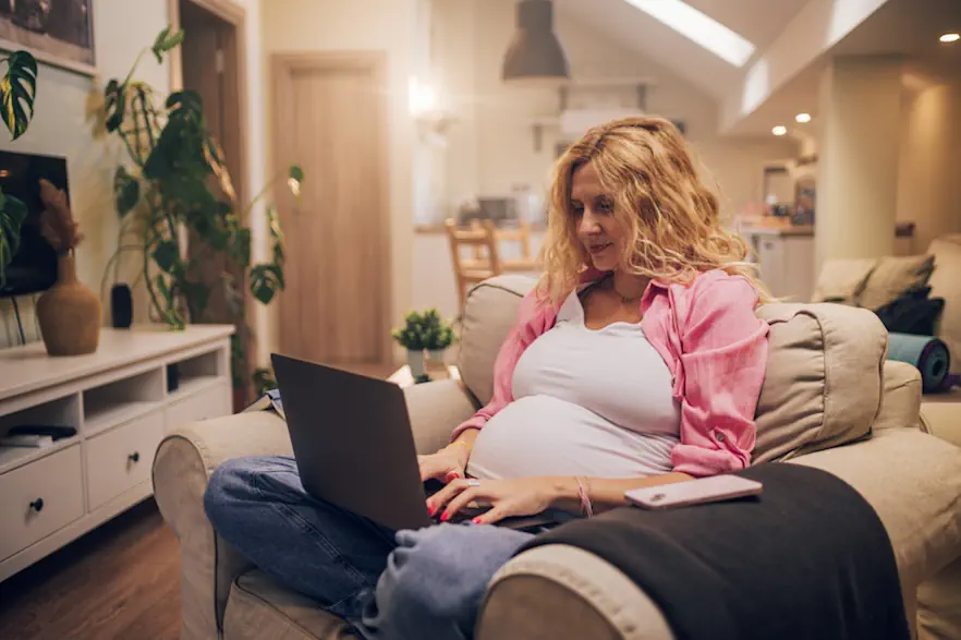 Schwanger Frau die gemütlich im Wohnzimmer am Laptop sitzt.