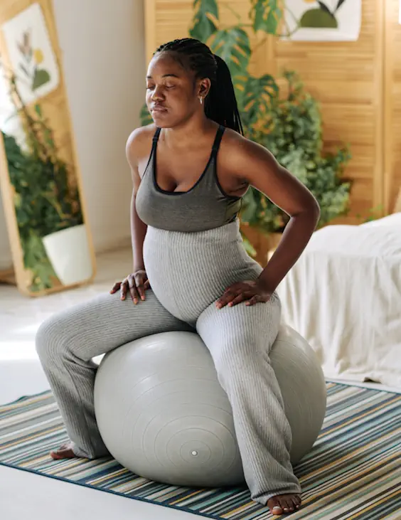 Schwangere sitzt auf einem Gymnastikball. Konzentriert, mit geschlossenen Augen bewegt und atmet sie sich durch die Wehen.